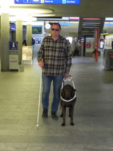 Arno Tschudi se déplace énormément avec son chien-guide Balou. Sur la photo il est a la gare de Coire