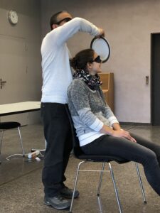 L'instructeur en O+M Juan Ruiz est debout derrière une femme assise sur une chaise, les yeux bandés. Il tient une assiette devant son visage. L'exercice consiste pour elle à repérer, grâce à des claquements de langue, de quel côté de son visage se trouve l'assiette. 