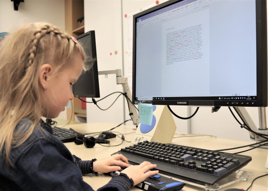 Lia Häfliger sitzt vor ihrem Computer und schreibt auf ihrer Braillezeile.