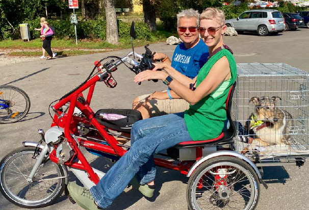 Alexandra und Robert Öllinger sitzen auf dem Tandem. Hinten auf dem Tandem ist eine Hundebox befestigt, in der der Blindenführhund sitzt. 