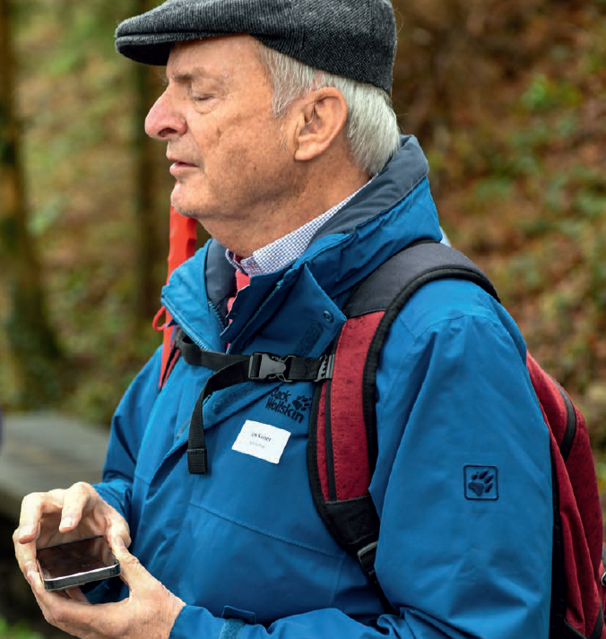 Ein Mann in Outdoor-Kleidern hält das iPhone flach vor sich. Er berührt den Bildschirm mit geschlossenen Augen und lauscht auf die Stimme des Telefons. 