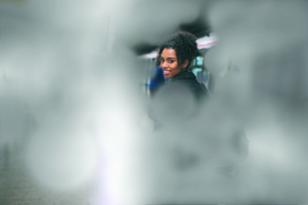 Une jeune femme, debout devant un train, regarde la caméra. L'image est traitée de manière à simuler la vision tubulaire.