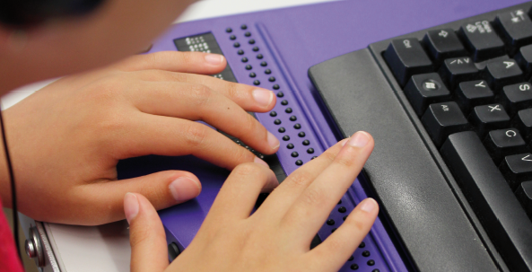 L'image montre les mains d'une personne sur une ligne braille. 