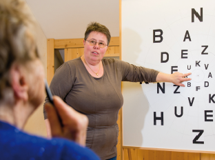 Das Bild zeigt Susanne Trefzer und eine Klientin vor einer Sehtafel. 