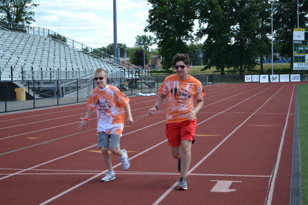 Das Bild zeigt zwei sehbeeinträchtigte Jugendliche, die im Leichtathletikstadion laufen.  