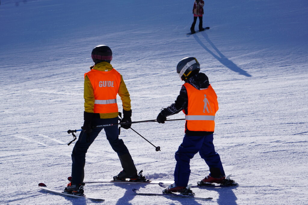 Das Bild zeigt einen Schüler, der mit einem Guide Ski fährt. 