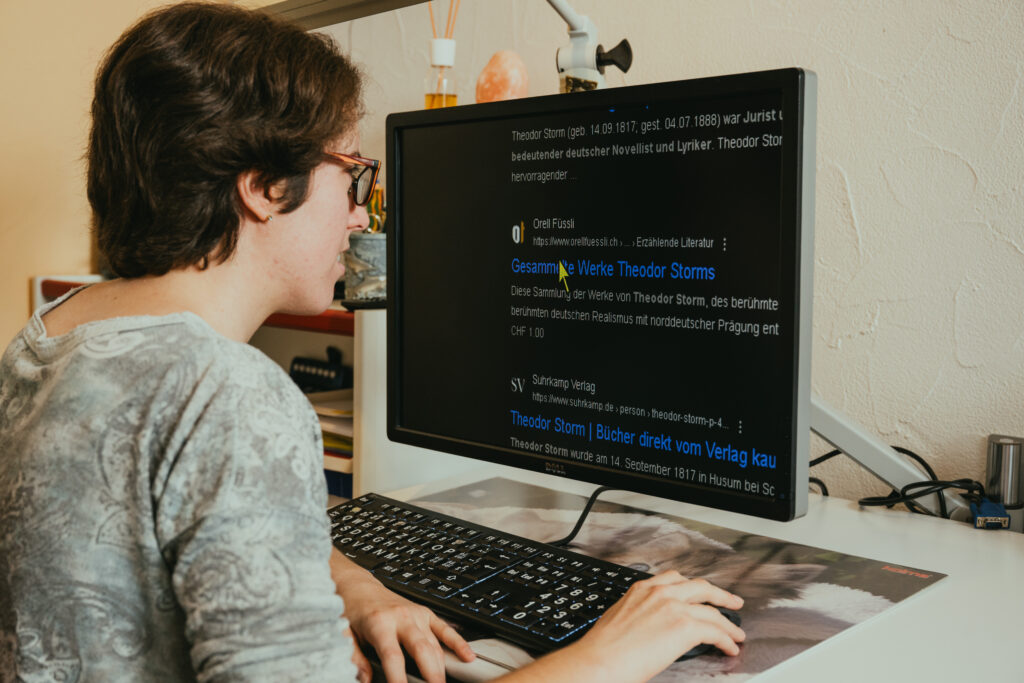 Assise à son bureau, une femme s’active sur son clavier à gros caractères. Un site d’informations sur l’écrivain Theodor Storm est affiché à l’écran. Le texte est agrandi.