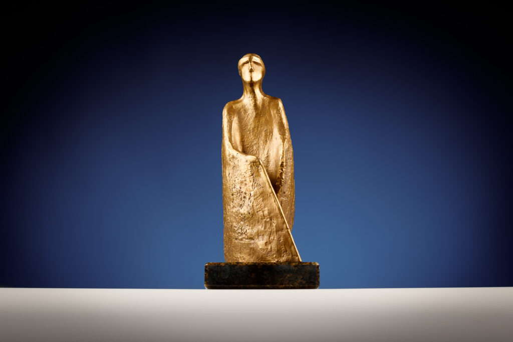 Sur fond bleu, la statuette dorée d’une personne tenant dans sa main droite une canne blanche.
